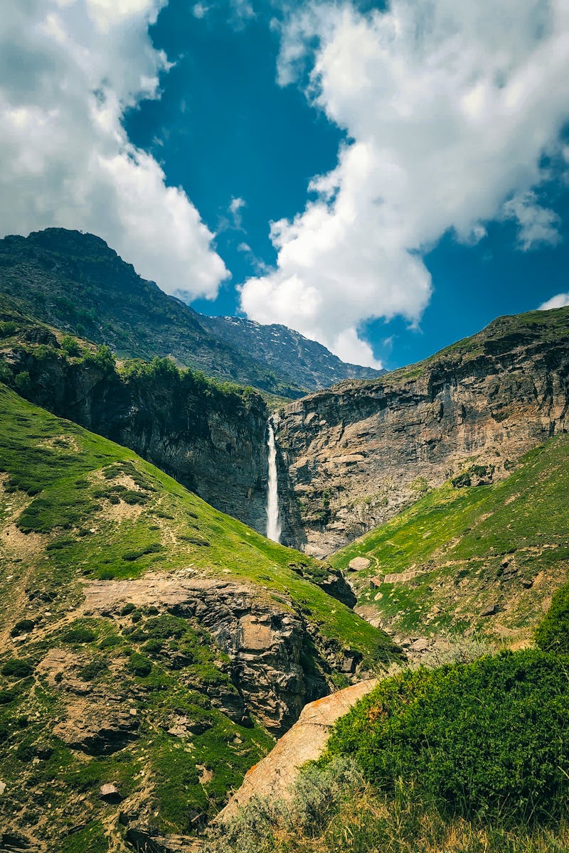 Stunning waterfall cascades down cliffs in Sissu, India under a vibrant blue sky.