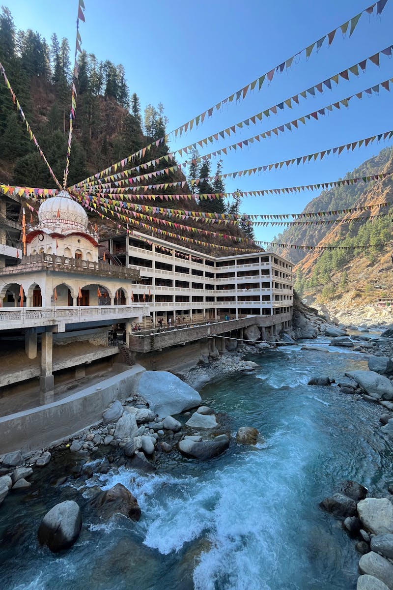 Colorful flags draped over Manikaran temple by a rushing river in Himachal Pradesh, India.